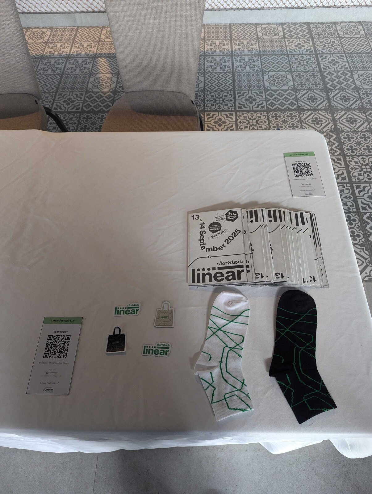 Top-down of the Linear merch table: metro-line socks, logo stickers, printed festival schedules and a scan-to-pay QR card